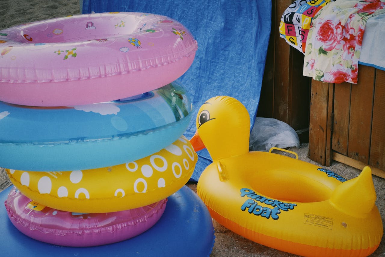 Vibrant inflatable rings and duck float on a sandy beach, perfect summer vibe.